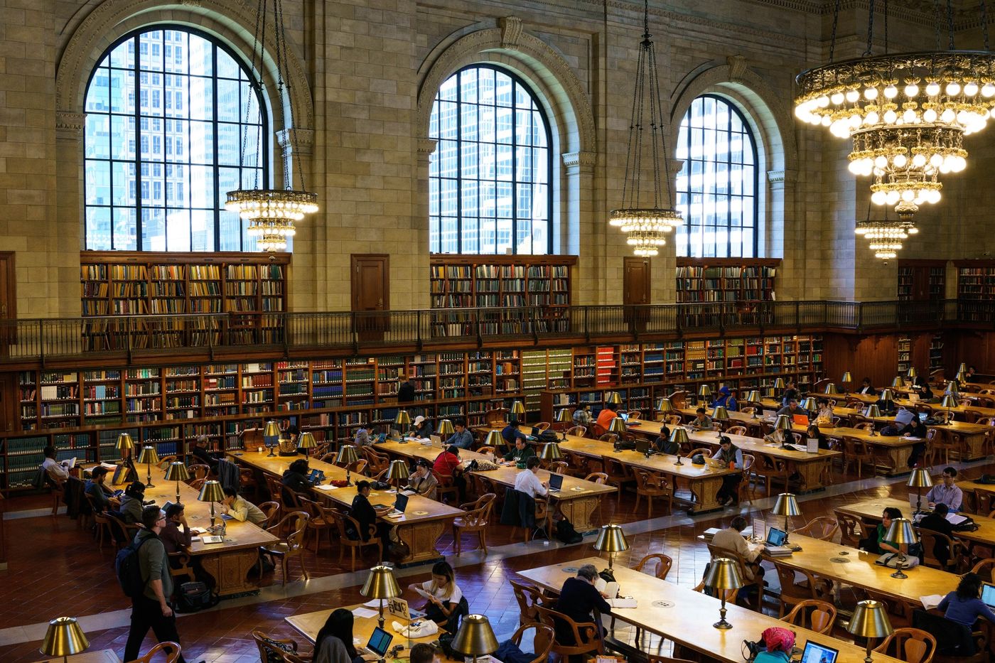 photo of a grand library (Boston? NYC?) with lots of working tables, lamps, chandeliers, and books lining the walls