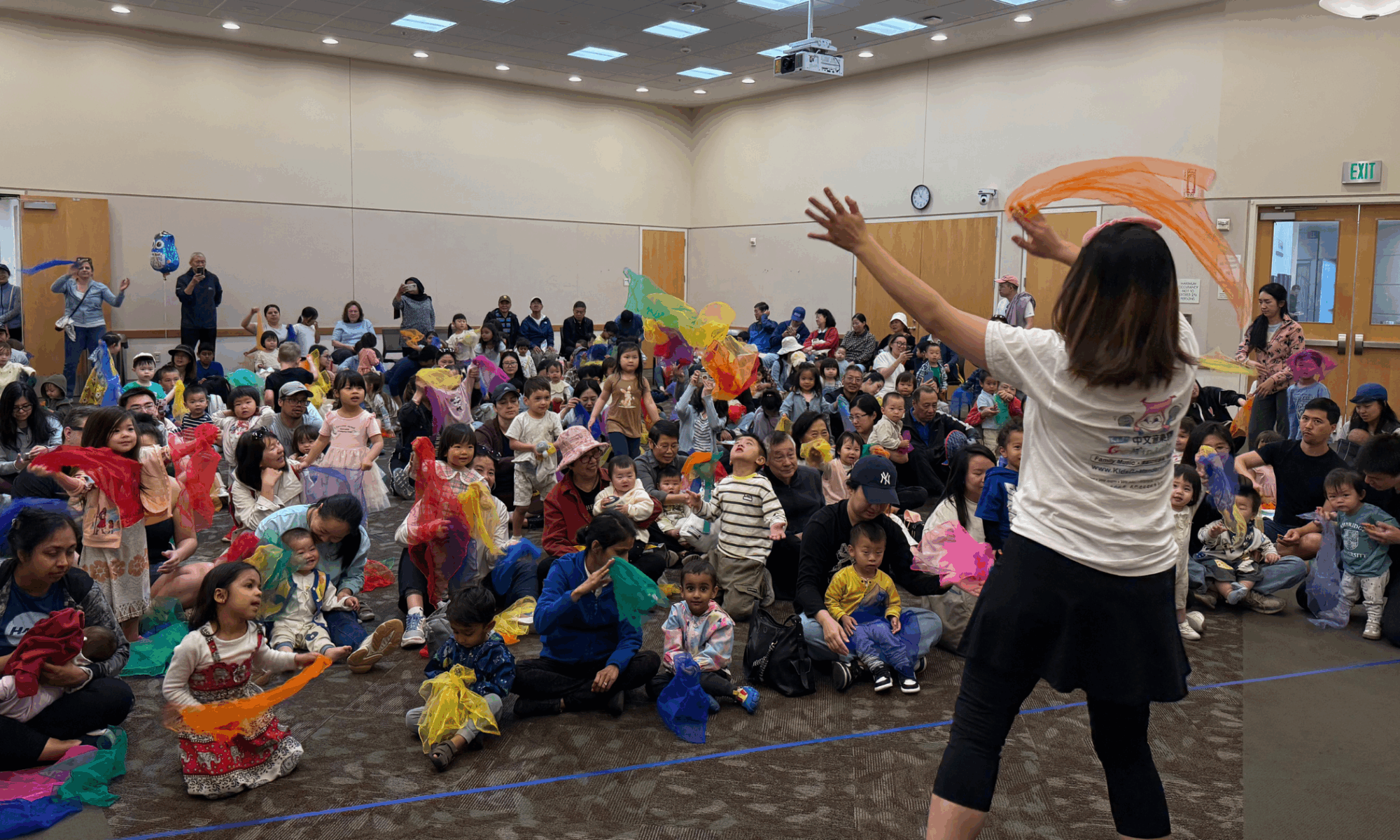 a group of children and their parents waving around brightly colored pieces of fabric at an event at the Santa Clara City Library